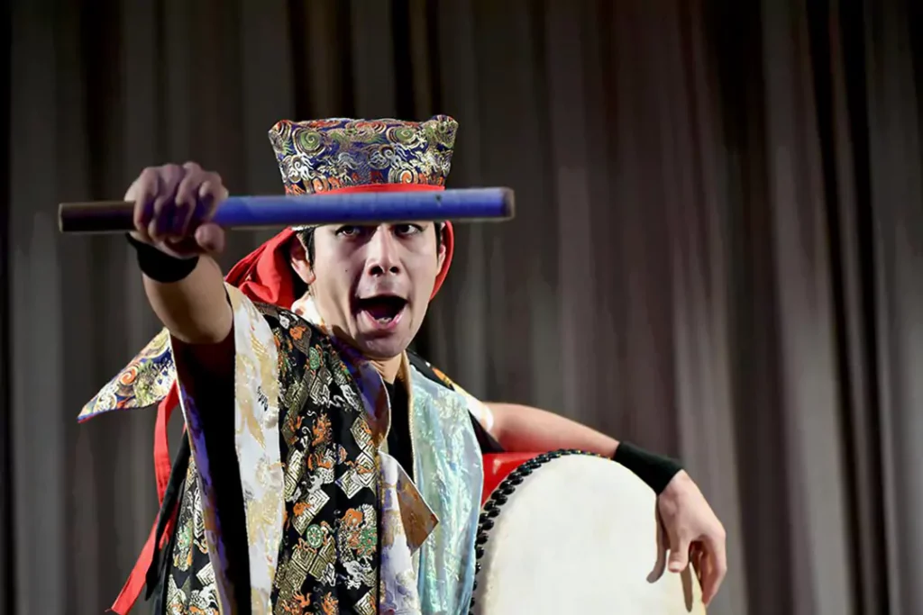 A dynamic shot of a taiko drummer striking the drum with high speed, creating motion blur under dramatic red lighting.