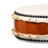 Close-up of JINLEI Hira Daiko Keyaki drum showing cowhide drumhead edge with double-row black bead tacking, natural rawhide lacing and warm reddish-brown keyaki wood grain shell