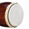 Side angle view of JINLEI Nagadou Daiko Kapiac drum showing cowhide drumhead with black bead tacking and rawhide lacing against deep burgundy kapiac wood shell