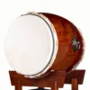 JINLEI O-Daiko Akatsuki Series side angle view showing large cowhide drumhead with black bead tacking, rawhide lacing and rich swirling wood grain shell on mahogany stand