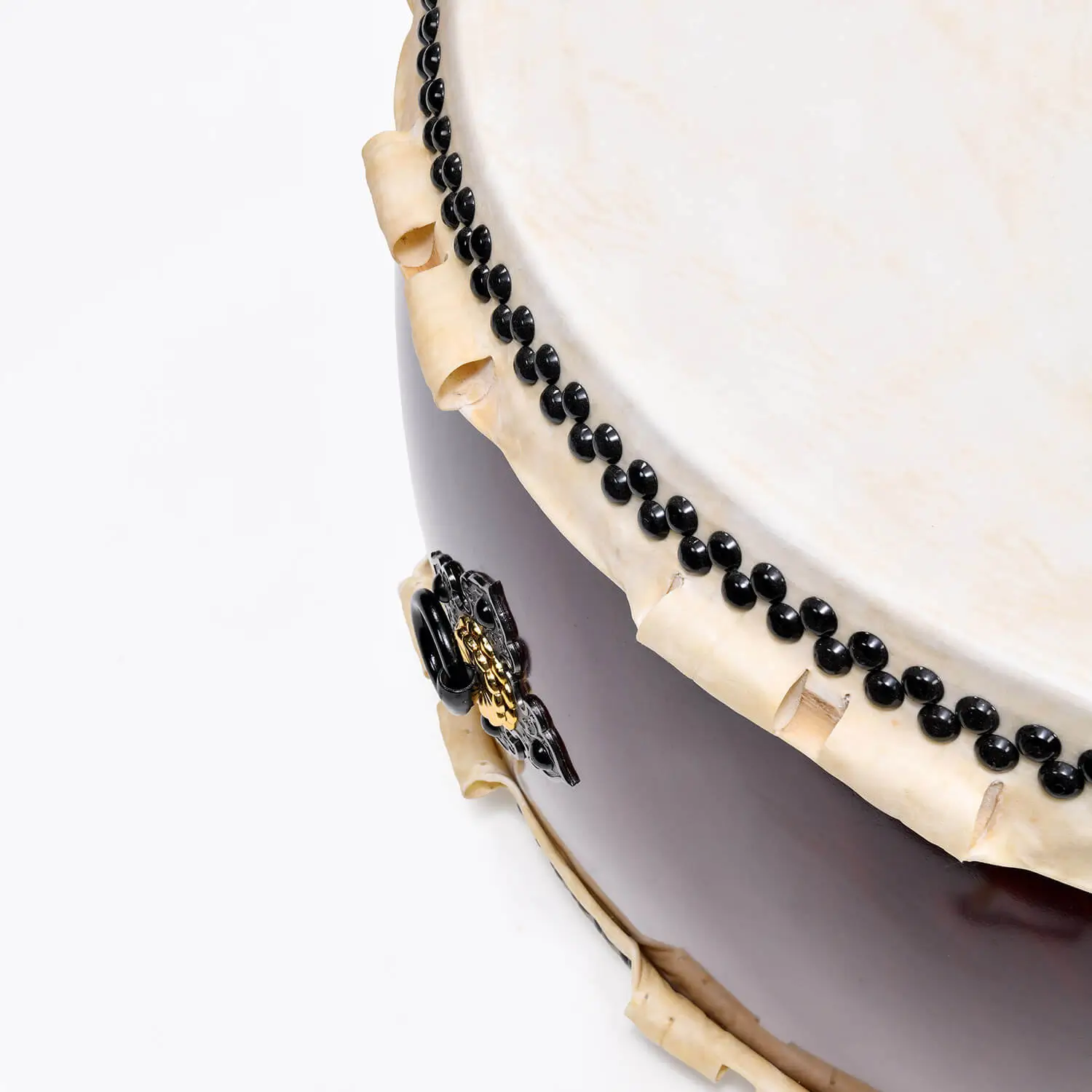 Close-up of JINLEI O Hira Daiko Kurinuki drum showing double-row black bead tacking, natural rawhide lacing and ornate black cast iron diamond hardware with gold accent on deep burgundy wood shell