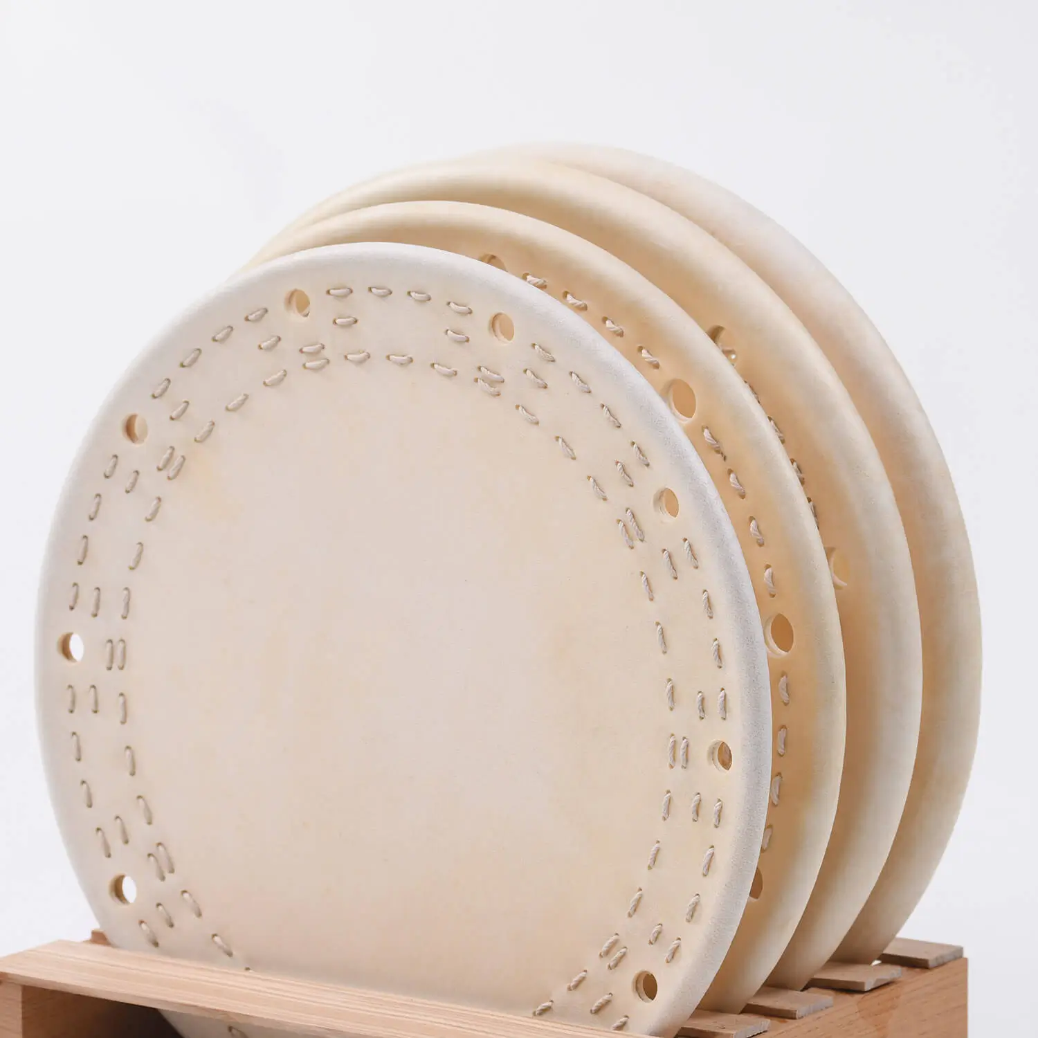 Close-up of JINLEI Shime Daiko Head showing four natural cowhide drumheads with hand-stitched leather rims and perforated edges stacked on wooden display rack