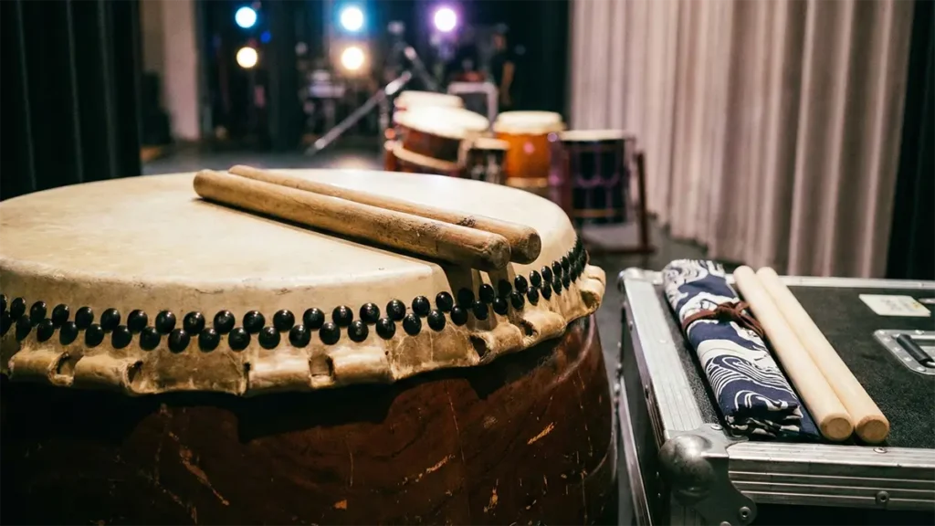 A pair of used wooden taiko bachi on a drumhead, with a new backup pair ready on a case beside them on stage.