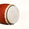 Side angle view of Nagado Daiko African Padauk hollowed-out solid wood drum showing cowhide drumhead with black bead tacking and vibrant red-brown padauk wood shell grain