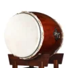 O-Daiko Kapiac Do Series side angle view showing large cowhide drumhead with black bead tacking, rawhide lacing and smooth reddish-brown kapiac wood grain shell on mahogany stand